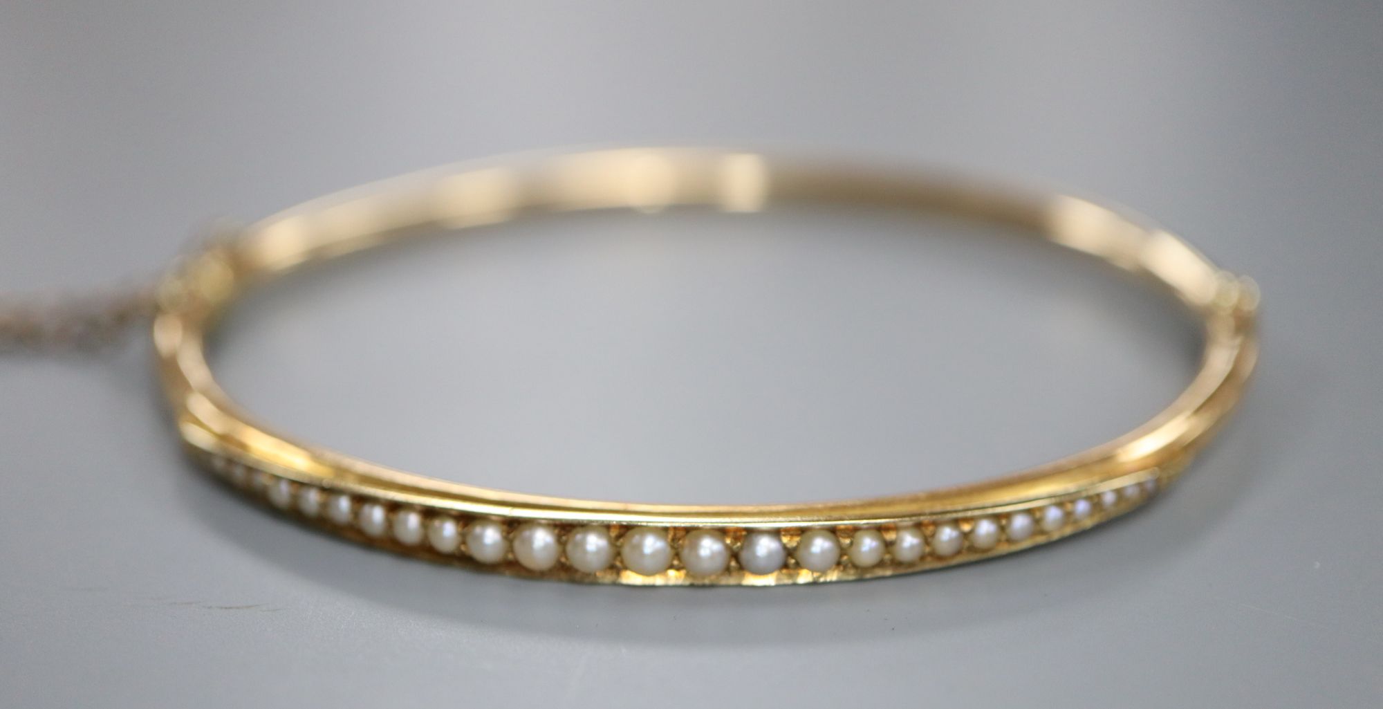 A cased Edwardian yellow metal and graduated seed pearl set hinged bracelet, interior 56mm, gross 6.4 grams.